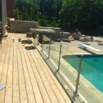 Glass pool fence installation near swimming pool with stainless steel posts.